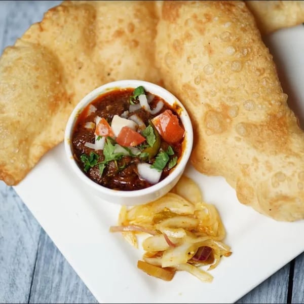 Clay Oven's Chole Bhature, featuring two golden fried bhature, chole, and pickled onions.