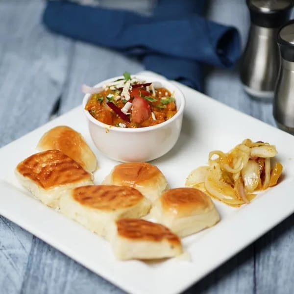 A white plate with Indian pav bhaji, small buns, and sautéed onions on a blue wooden table.